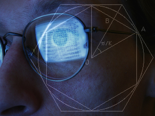 A man looks at a computer screen, reflected in his glasses. A geometrical diagram is superimposed over the photo.