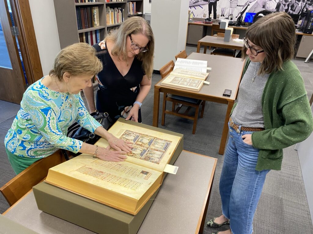Dr. Annette Cash browses pages of illustrations from the book "Cantigas de Santa María" with Christina Zamon, Department Head of Special Collections and Archives, and library associate Lydia Brown.