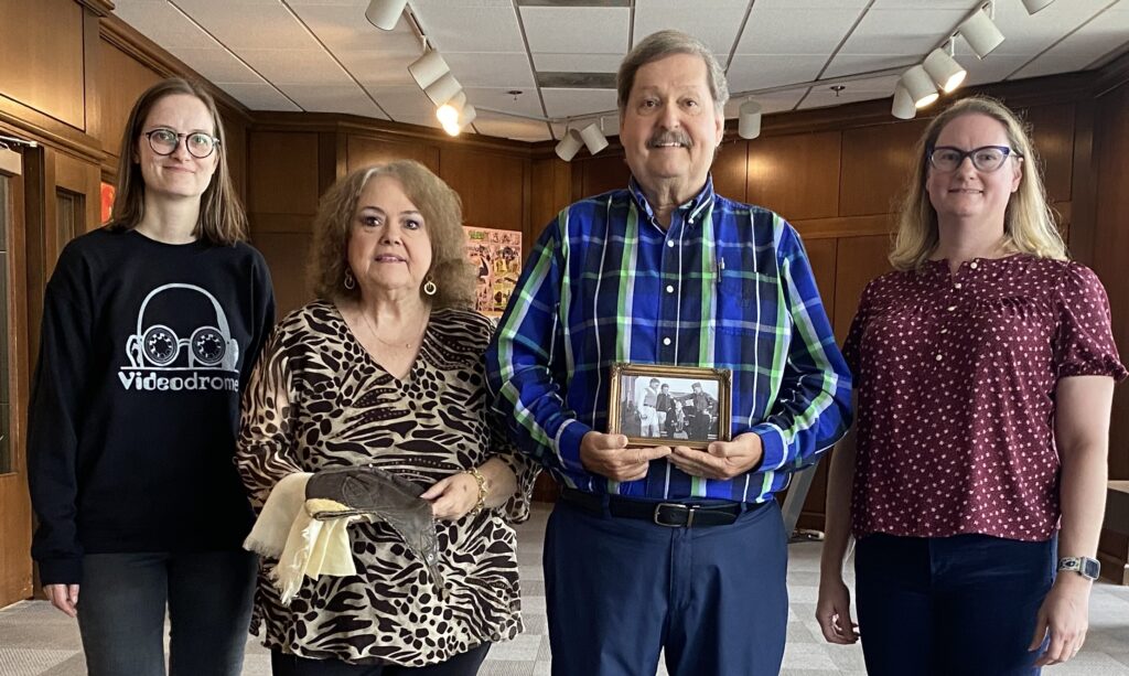 Dan Brown holds a photo of his father with Amelia Earhart. Brown’s wife (second from left) holds his father’s flight cap and scarf.